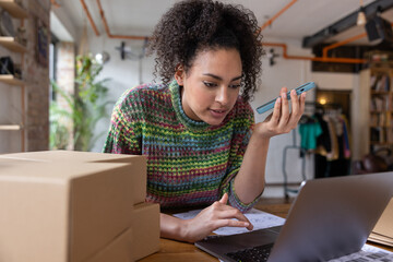 African American female entrepreneur looking at order details from e-commerce site and speaking on phone