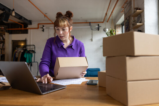 Trendy young female entrepreneur looking at order details from e-commerce site on a laptop computer