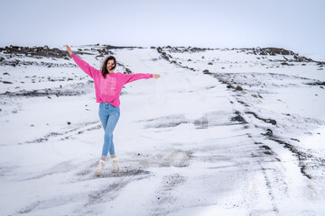 a girl in pink standing on a snow covered road and raising her arms
