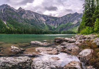 A landscape scene of a lake in a deep mountain valley with rocks submerged in the foreground,...