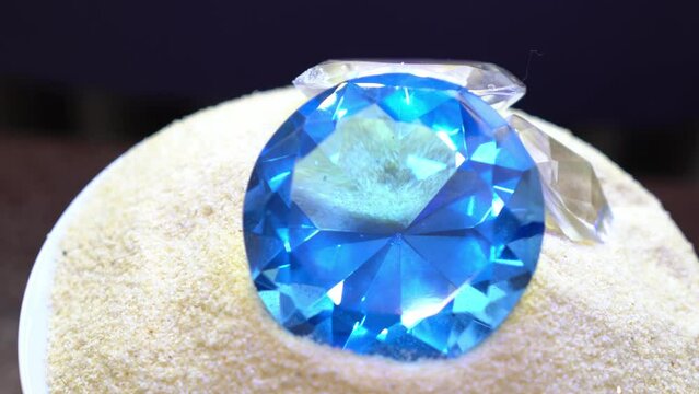 Closeup footage of three white and blue diamond-shape crystals on sand rotating on a blur background