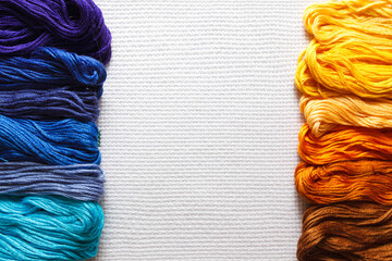 Threads of different shades of orange and blue on white fabric. 