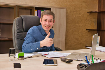 A man with a content expression sitting at a desk, enthusiastically giving a thumbs up gesture