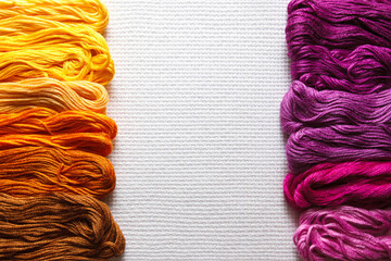 Threads of different shades of orange and purple on a white fabric. 