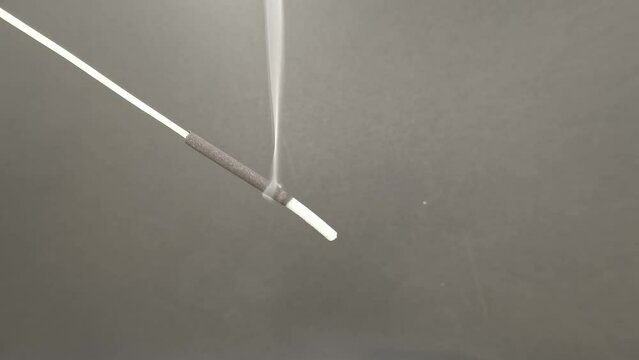 Closeup shot of the white incense smoke rising from a burning bakhoor stick on a blur background