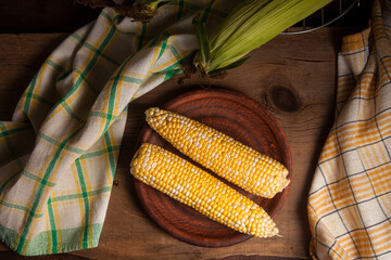 Clay plate with two cobs sweet corn on wooden background..
