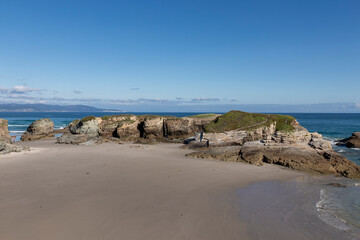 A serene beach with rocky formations, clear blue skies, and calm waters, evoking a sense of tranquility and natural beauty in asturias
