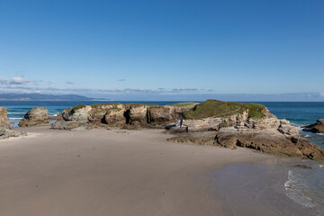 A serene beach with rocky formations, clear blue skies, and calm waters, evoking a sense of...