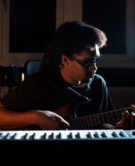 black african blind man musician playing guitar recording in production studio with piano
