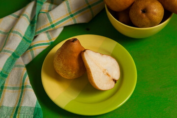 Green plate with whole and half of pear and green kitchen towel on green wooden background..
