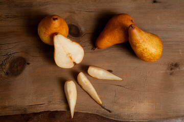Whole, half and slices of pears on wooden background with yellow kitchen towel..