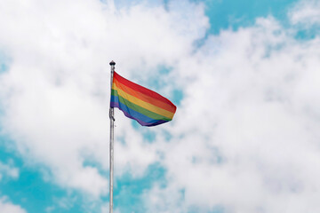 waving rainbow pride flag in cloudy sky 