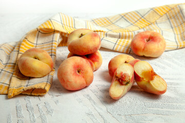 Halves and several whole saturn peaches or flat peach on white wooden background..