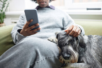 Close up of woman relaxing on couch with dog and scrolling social media via smartphone, copy space