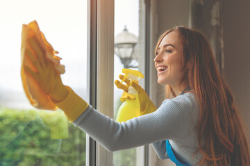 joyful woman in protective gloves washing window in living room Cleaning service and housework...