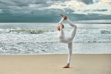 Young hairless ballerina with alopecia in white futuristic suit dancing on sea sandy beach,...