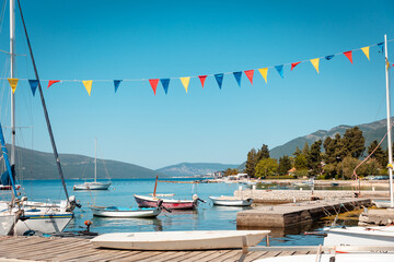Beautiful sunny view of village pier with boats and flags on the Mediterranean coast. Summer...