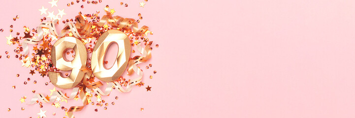 Banner with gold colored number 90, ribbons and stars confetti on a pink background.