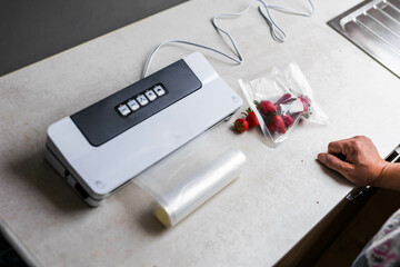 a man's hand is using a vacuum machine to vacuum pack strawberries into plastic bags.