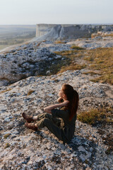Woman sitting on cliff edge overlooking valley and mountains on travel adventure trip to nature beauty