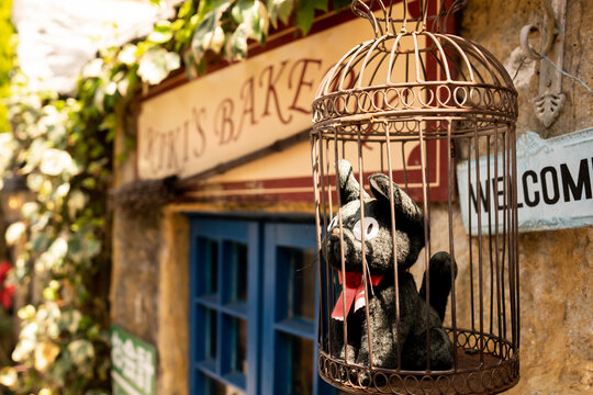 JAPAN - APR 17, 2024: A charming black cat plush toy placed inside a decorative birdcage outside the entrance of Kiki's Bakery, surrounded by lush greenery in Yufuin Floral Village, Fukuoka