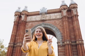 Young female tourist visiting Barcelona triumphal arch. Traveling woman taking selfie outdoors. Banner of travel, tourism and vacation in city. Use technology concept, Traveling Europe