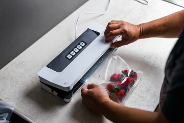 a man's hand is using a vacuum machine to vacuum pack strawberries into plastic bags.