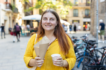 Carefree woman eating traditional Churros, a fried pastry with chocolate on a city street. Positive cheerful female student posing outdoors. Food concept