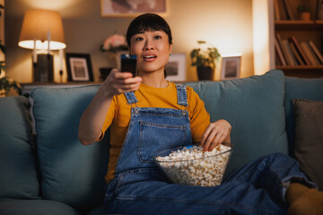 Woman using remote control switching channals while watching TV at home