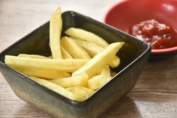 French fries mixed with salt in cup dipping ketchup on table  