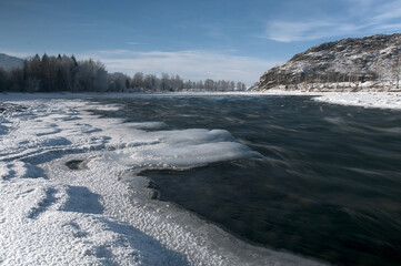 A frozen river bank with a distant mountain under a cloudy sky
