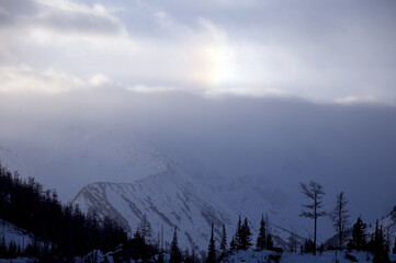 Sunlight breaks through clouds above snowcovered mountains.