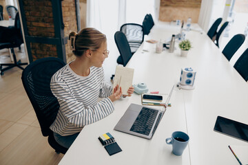 Female freelancer showing something to client in note pad during video conference in coworking