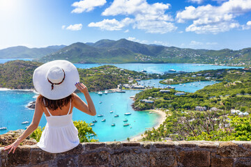 A tourist woman in a white dress enjoys the panoramic view over the landscape of Antigua island...
