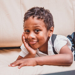 a close-up portrait of a boy lying on a sofa on his stomach, propping his chin up with his hand and...