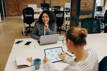 Group of female managers sitting in open modern office while working on laptop and digital tablet