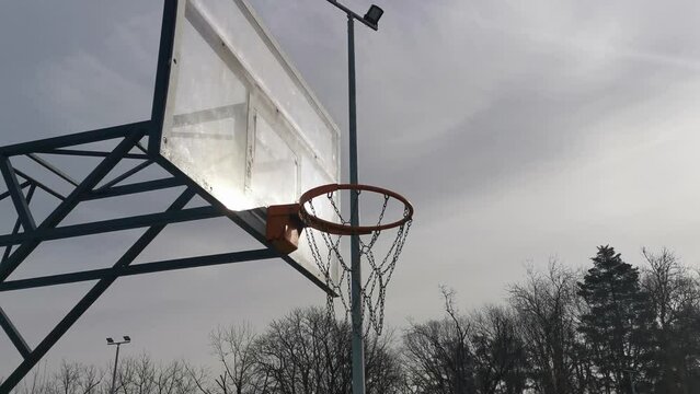 A basketball net under a cloudy sky. The back board has been busted and is now covered with a large piece of wood.