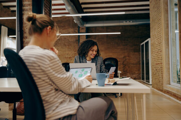 Group of female managers sitting in open office while working on digital tablet and laptop