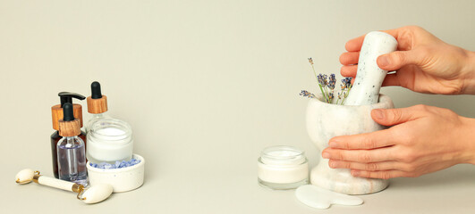 Lavender, sea salt, massagers, female hands, cosmetic bottles and jars on gray background, space for text