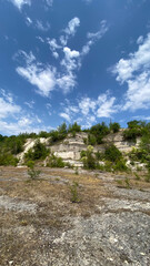 Rocky hillside with scattered greenery under a vibrant blue sky with white clouds. Natural, serene outdoor landscape