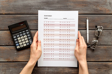 Female hand with answer exam sheet form on a table, top view. Education background