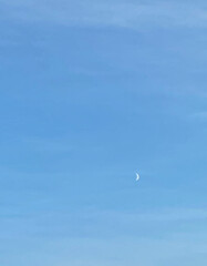 Clear blue sky with a crescent moon during the daytime. Minimalistic and serene natural scene...