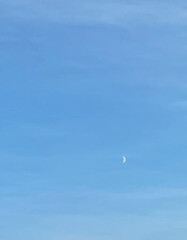 Clear blue sky with a crescent moon during the daytime. Minimalistic and serene natural scene capturing the beauty of the sky and moon