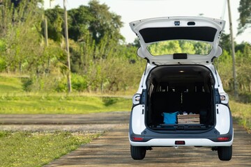 The rear view of a white car with an open trunk full of luggage on a rural road.