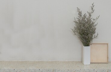 A minimalist still life image of a vase of dried flowers on a concrete table against a beige wall...