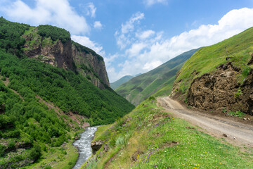 Terek river and earthen road in a gorge between mountains among rocks. Green grass and bushes around