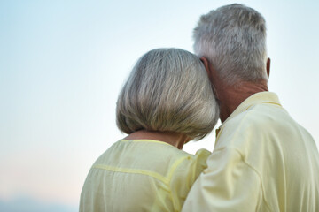 Fototapeta premium Happy elderly couple hugging against sky background