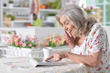 Portrait of beautiful senior woman using modern tablet while drinking tea
