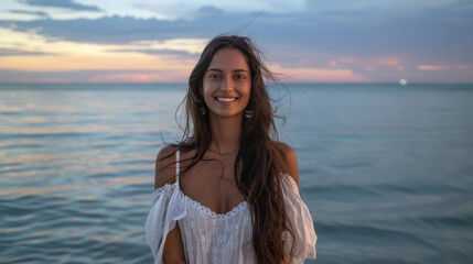 Beautiful indian lady in brown long hair and white dress, standing in front of the sea