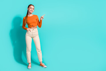 Full size photo of cute girl with ginger hair dressed orange shirt indicating at promotion empty space isolated on teal color background